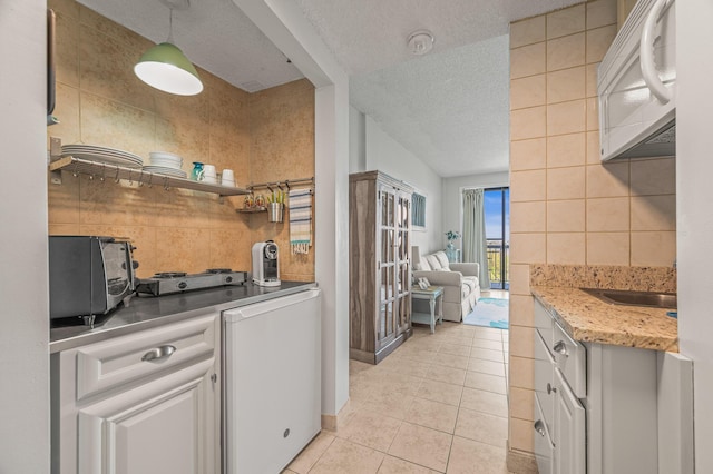 kitchen with light tile patterned floors, light countertops, a textured ceiling, open shelves, and tile walls