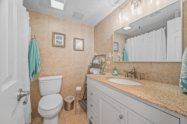 bathroom with a textured ceiling, vanity, tile patterned flooring, toilet, and tile walls