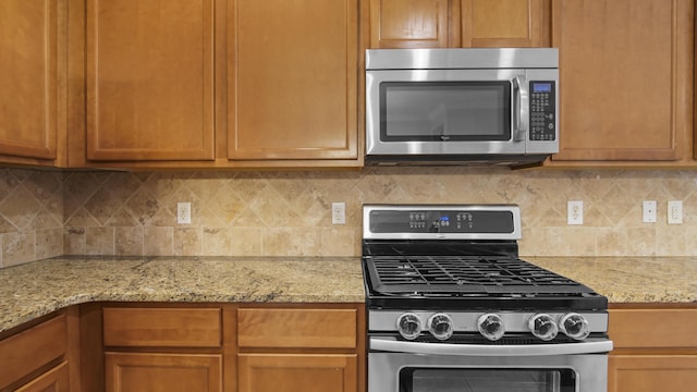 317 Turtle Cv, Panama City Beach, FL 32413 - kitchen with brown cabinets, decorative backsplash, light stone counters, and appliances with stainless steel finishes