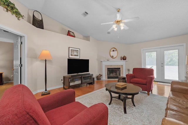 living area featuring light wood-style floors, a ceiling fan, visible vents, a tile fireplace, and french doors