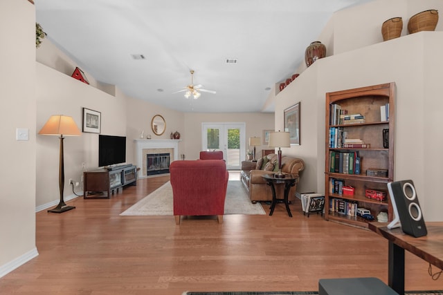 living room featuring wood finished floors, a glass covered fireplace, a ceiling fan, and visible vents