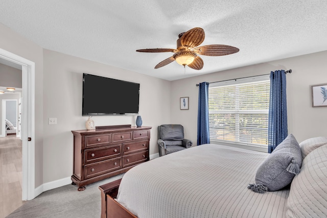 bedroom featuring baseboards, a textured ceiling, ceiling fan, and light carpet