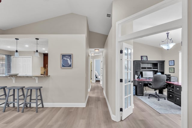 interior space featuring light stone counters, visible vents, a kitchen breakfast bar, light wood-style flooring, and vaulted ceiling