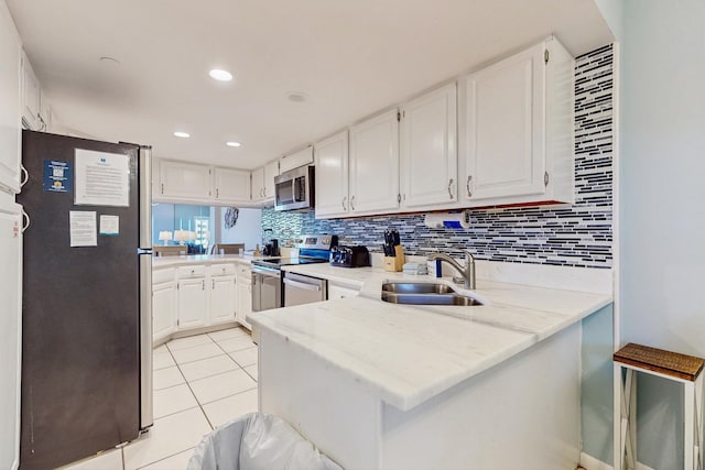 kitchen featuring a peninsula, white cabinetry, backsplash, appliances with stainless steel finishes, and a sink