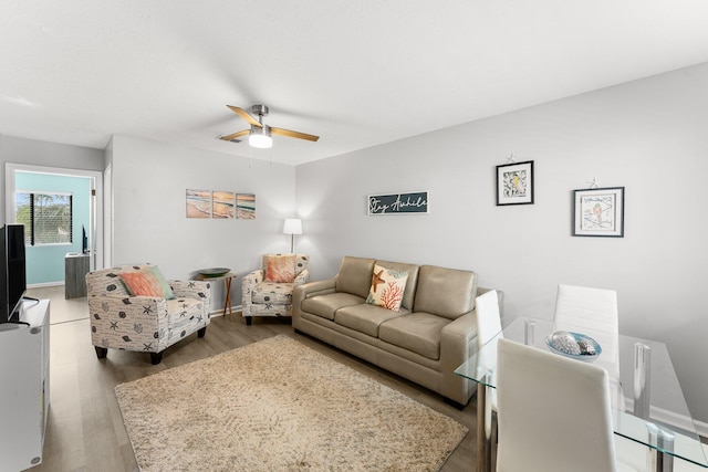 living area with baseboards, wood finished floors, and ceiling fan