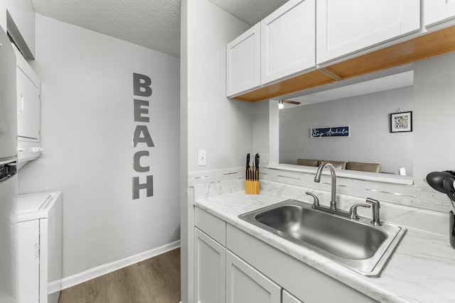 kitchen with a sink, a textured ceiling, stacked washer and dryer, dark wood-style floors, and white cabinetry