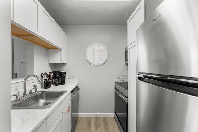 kitchen with white cabinets, a sink, appliances with stainless steel finishes, a textured ceiling, and light wood-style flooring