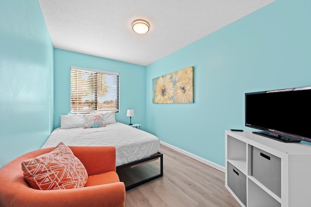 bedroom featuring baseboards, wood finished floors, and a textured ceiling