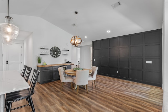 dining space with visible vents, an inviting chandelier, vaulted ceiling, dark wood-type flooring, and a decorative wall
