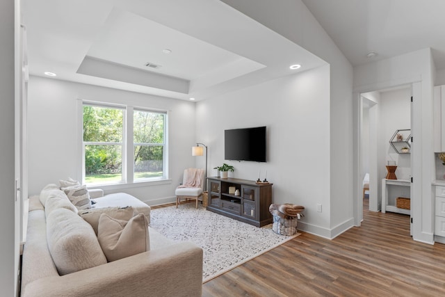 living area featuring recessed lighting, wood finished floors, baseboards, visible vents, and a raised ceiling
