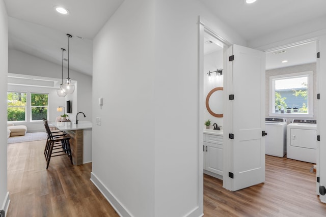 hall featuring wood finished floors, separate washer and dryer, vaulted ceiling, and recessed lighting