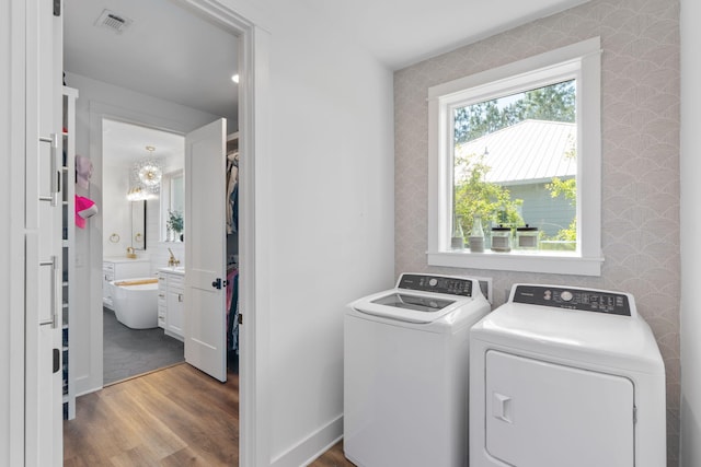 clothes washing area with wood finished floors, laundry area, wallpapered walls, visible vents, and washer and clothes dryer
