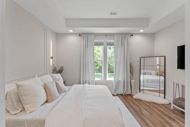 bedroom featuring baseboards, recessed lighting, wood finished floors, and a raised ceiling