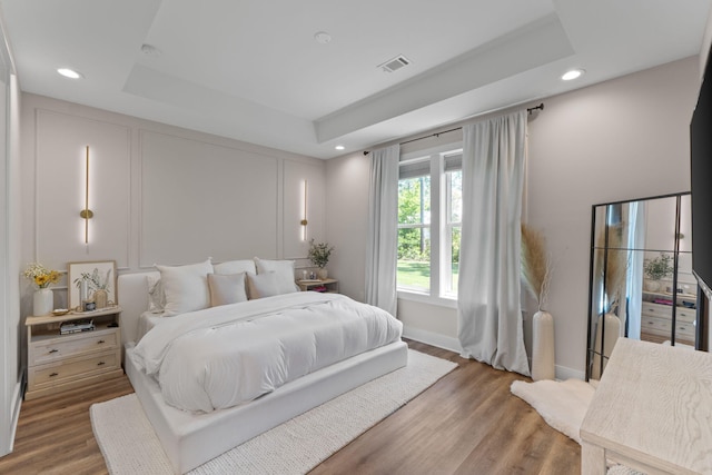 bedroom with recessed lighting, a raised ceiling, visible vents, baseboards, and wood finished floors
