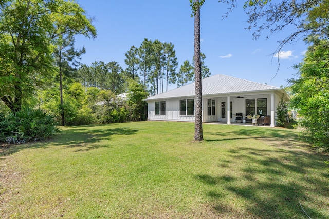rear view of house with board and batten siding, ceiling fan, metal roof, a patio, and a lawn