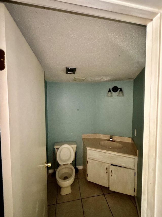 half bathroom featuring baseboards, toilet, a textured ceiling, vanity, and tile patterned floors
