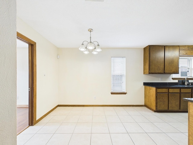 kitchen with hanging light fixtures, baseboards, a sink, dark countertops, and a chandelier