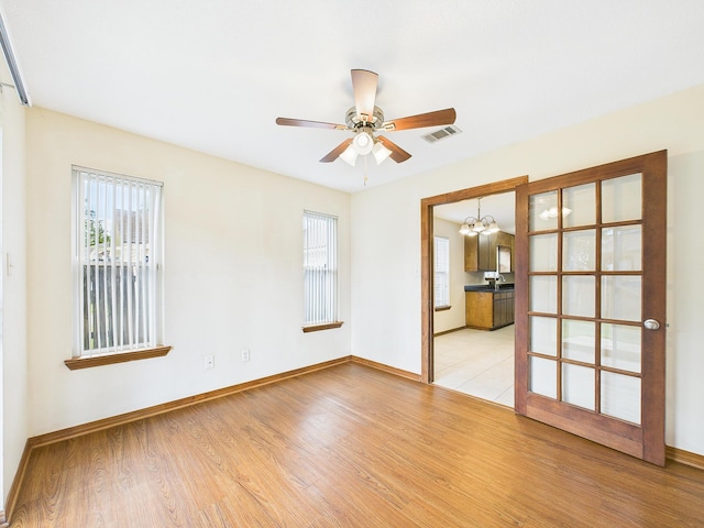 unfurnished room featuring light wood-style floors, visible vents, ceiling fan with notable chandelier, and baseboards
