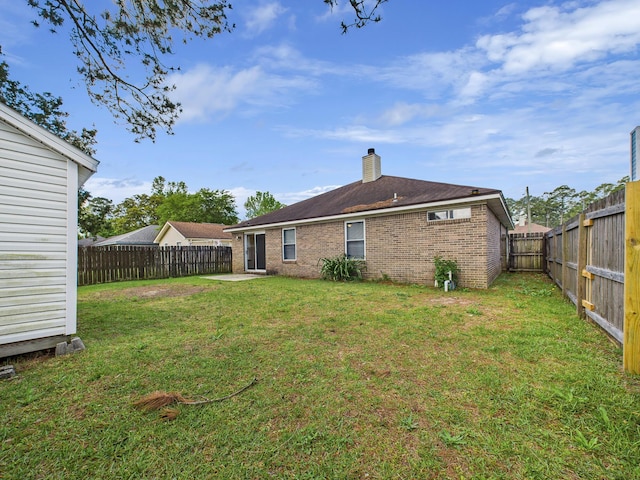 back of house with brick siding, a yard, a fenced backyard, and a chimney