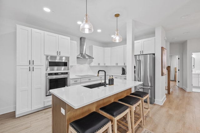34 Gulf Breeze Ct, Destin, FL 32541 - kitchen featuring wall chimney exhaust hood, a breakfast bar area, stainless steel appliances, light wood finished floors, and a sink