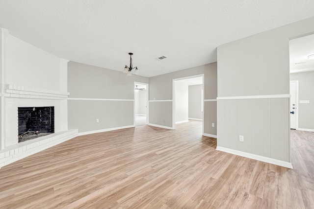 5700 Country Squire Dr, Milton, FL 32570 - unfurnished living room featuring an inviting chandelier, a fireplace, light wood-type flooring, a textured ceiling, and visible vents