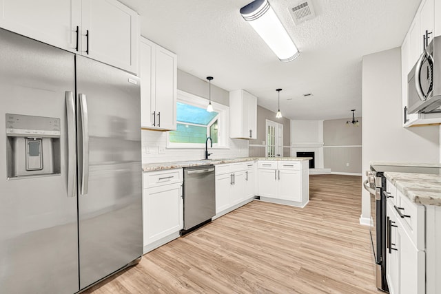 5700 Country Squire Dr, Milton, FL 32570 - kitchen featuring white cabinets, a fireplace with raised hearth, appliances with stainless steel finishes, light wood-style floors, and a peninsula
