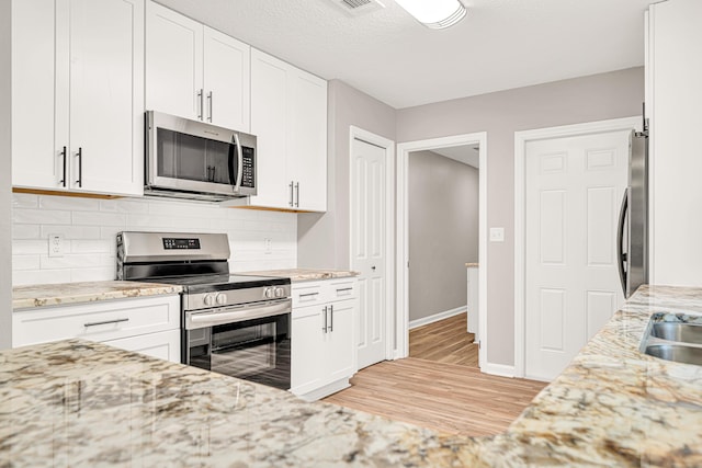 5700 Country Squire Dr, Milton, FL 32570 - kitchen featuring light wood-style floors, light stone countertops, tasteful backsplash, white cabinetry, and appliances with stainless steel finishes