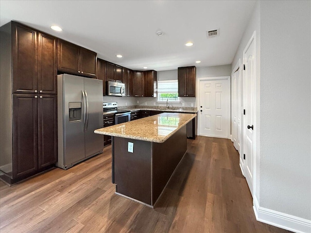 2055 Bright Water Dr, Gulf Breeze, FL 32563 - kitchen with appliances with stainless steel finishes, dark brown cabinetry, dark wood-style flooring, a center island, and light stone countertops