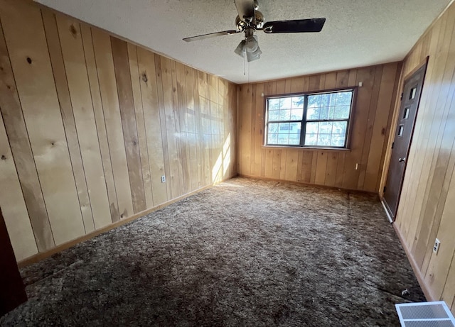 empty room with wood walls, visible vents, a ceiling fan, a textured ceiling, and carpet flooring