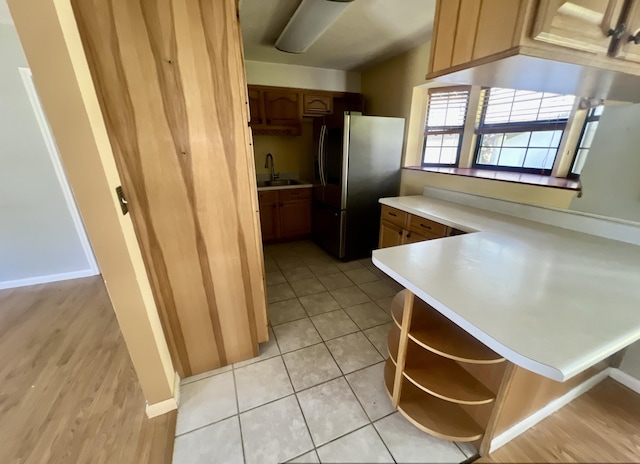 kitchen with stainless steel fridge with ice dispenser, a peninsula, open shelves, a sink, and light countertops