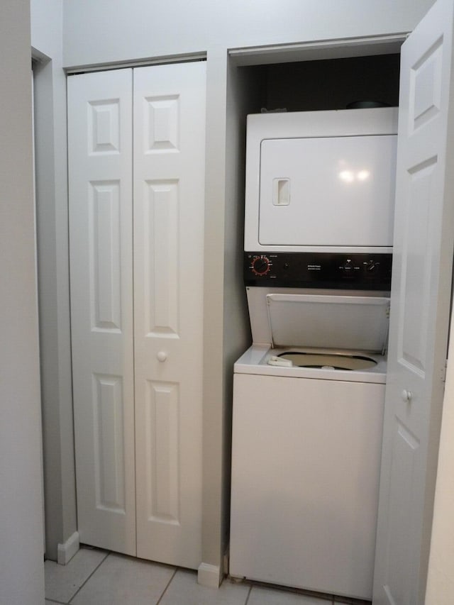 laundry area featuring laundry area, stacked washer and clothes dryer, baseboards, and light tile patterned floors