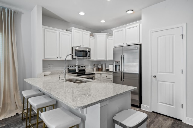 kitchen featuring a sink, a peninsula, white cabinetry, stainless steel appliances, and light stone counters