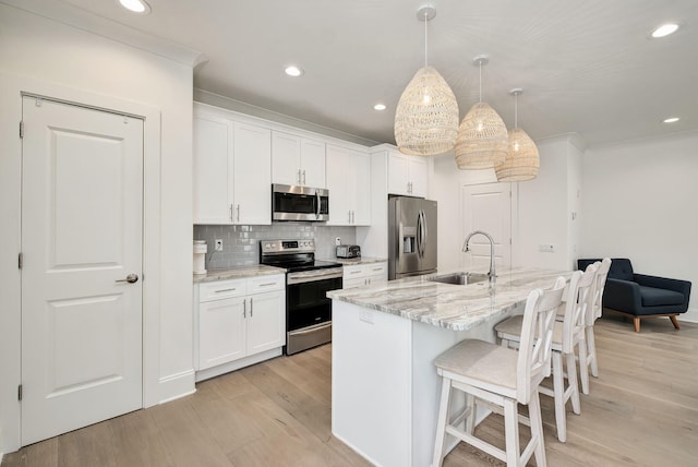 kitchen with light wood-style floors, appliances with stainless steel finishes, a sink, white cabinetry, and a kitchen breakfast bar