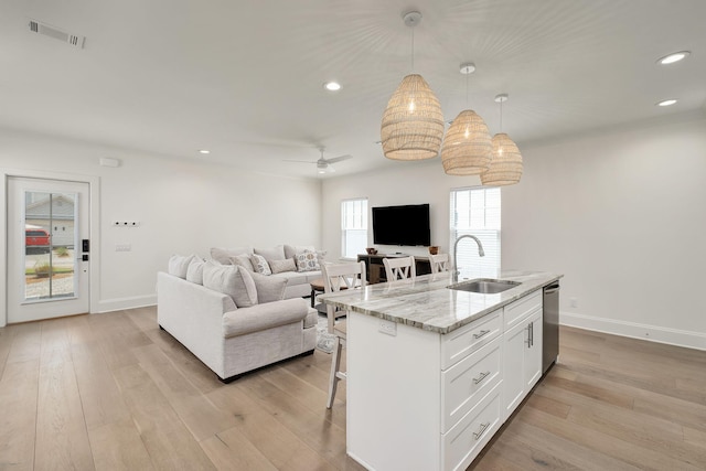 kitchen with an island with sink, a breakfast bar, white cabinets, dishwasher, and a sink
