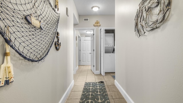 hall featuring light tile patterned flooring, stacked washer / drying machine, visible vents, and baseboards