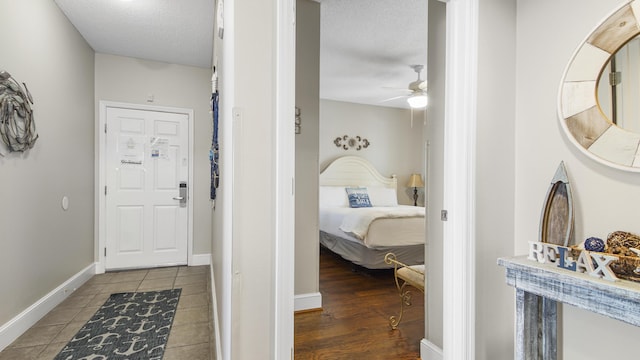 hallway featuring a textured ceiling, tile patterned floors, and baseboards