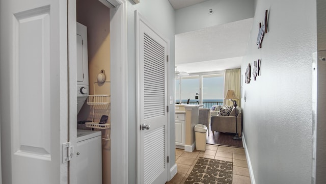 hall featuring baseboards, light tile patterned floors, stacked washer and dryer, and a water view