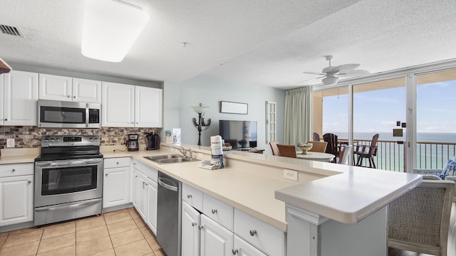 kitchen with appliances with stainless steel finishes, backsplash, a sink, visible vents, and a peninsula