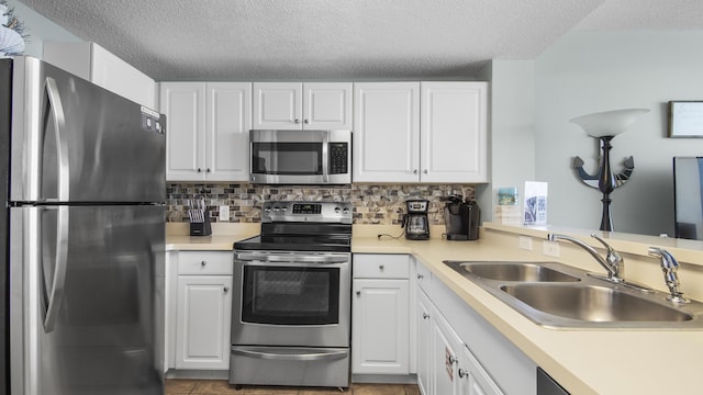 kitchen with a textured ceiling, decorative backsplash, white cabinets, a sink, and appliances with stainless steel finishes