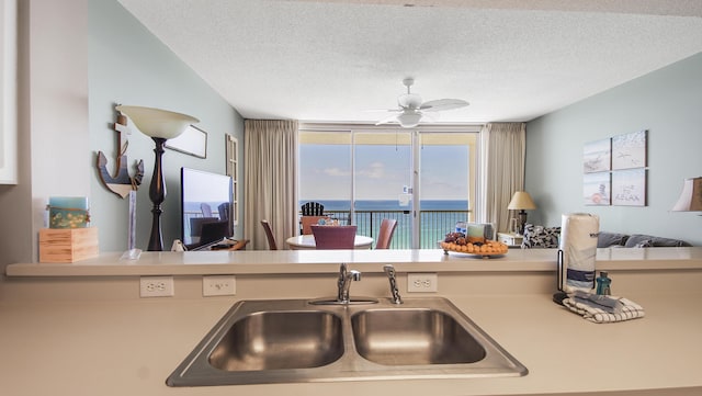 kitchen with light countertops, ceiling fan, a sink, a textured ceiling, and open floor plan