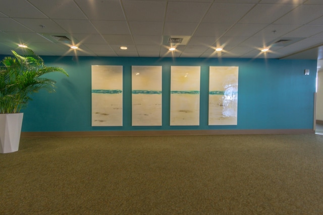 empty room with carpet flooring, a drop ceiling, and baseboards