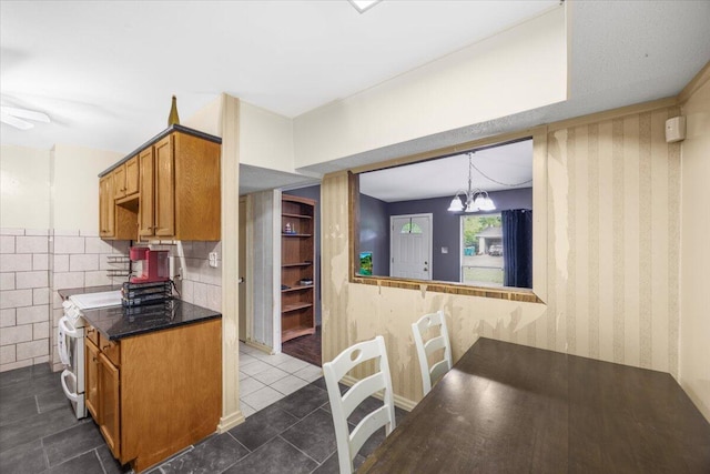 706 Mary Ave, Fort Walton Beach, FL 32547 - kitchen with electric stove, dark tile patterned floors, brown cabinetry, wallpapered walls, and dark countertops