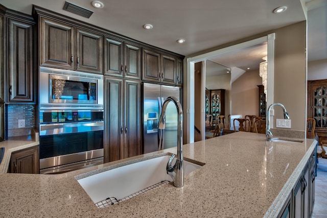 kitchen featuring a sink, light stone counters, dark brown cabinetry, and stainless steel appliances