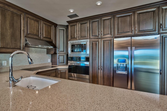kitchen with visible vents, dark brown cabinets, light stone counters, a sink, and appliances with stainless steel finishes