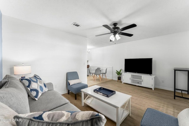 living room with visible vents, baseboards, wood finished floors, and ceiling fan