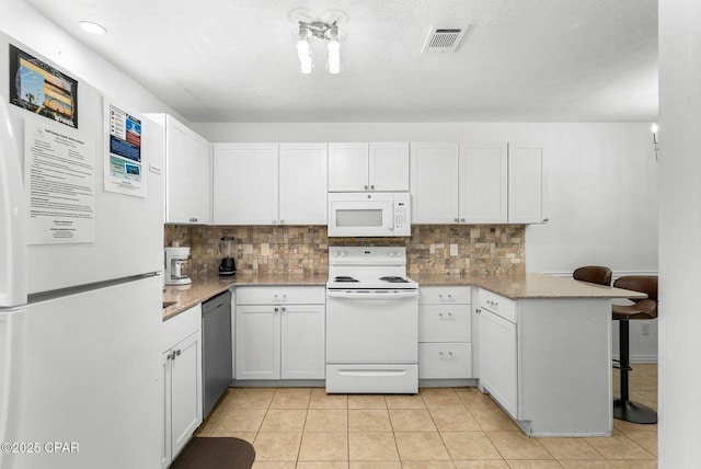 kitchen with a peninsula, backsplash, white appliances, and visible vents