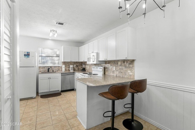 kitchen with visible vents, a sink, white appliances, white cabinetry, and backsplash