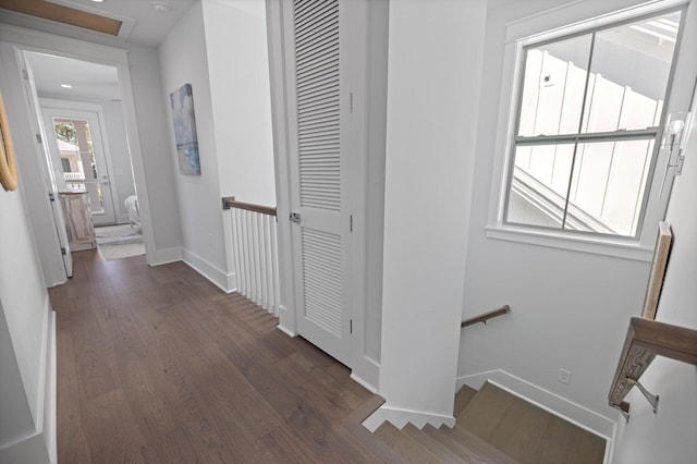 corridor with baseboards, an upstairs landing, and dark wood-style flooring