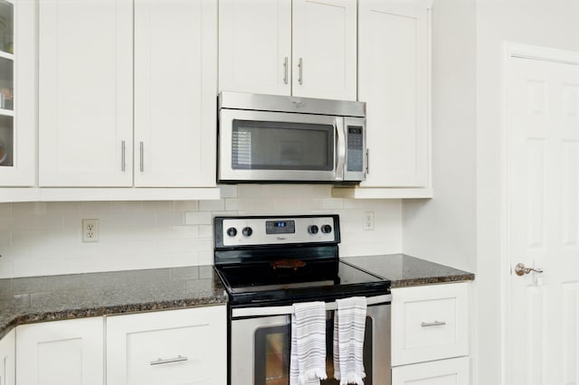 kitchen with dark stone counters, decorative backsplash, glass insert cabinets, white cabinets, and appliances with stainless steel finishes