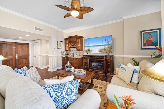 living room featuring dark wood-style flooring, crown molding, ceiling fan, and a wainscoted wall